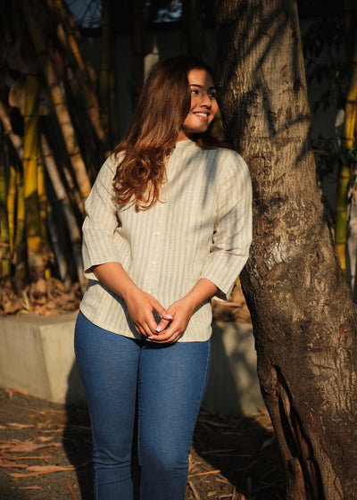 woman in a beige shirt leaning against a tree